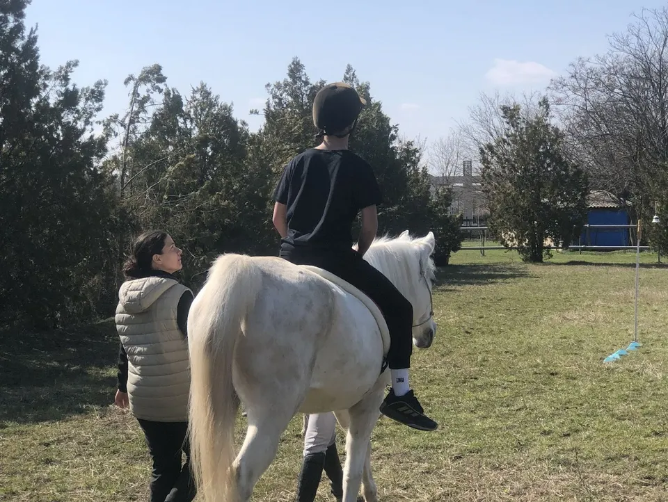 Un copil călare, asistat de un adult